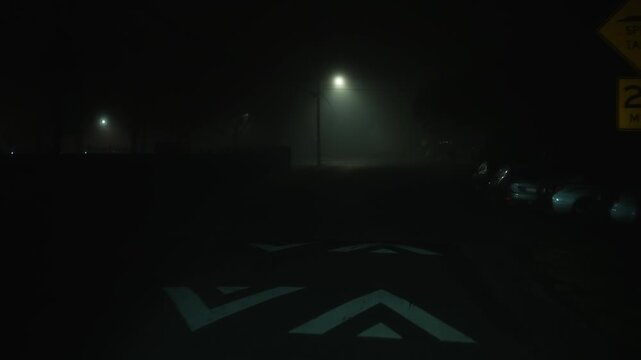 Driving along foggy night street with speed limit sign, forward motion on empty road through dense fog creates atmosphere of low visibility night driving and heightened caution