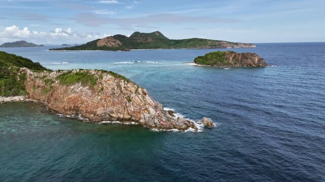 POI drone shot of a rocky cape at Ile Island with expansive ocean views and Kinulay and Patoyo Islands in the background, Philippines