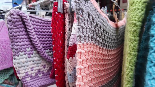 Colorful knitted clothes and crochet accessories hanging on metal rack at outdoor market.