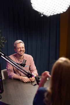 Announcer recording audio podcast during live broadcasting in studio. Host speaks into microphone, engaging in conversation with guest, producing digital content for online blog or streaming channel