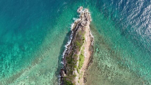 Riser helix drone shot circling a rocky cape at Ile Island, highlighting turquoise waters and gentle waves along the coastal reef, Philippines