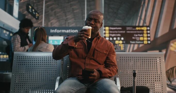 Black Man Sits in Airport Lounge, Using Smartphone Scan QR Code on Ticket. While Waiting Flight, Male Traveler Drinks Cup of Coffee, Calmly Double Checks Departure Details. Modern Travel Technology.