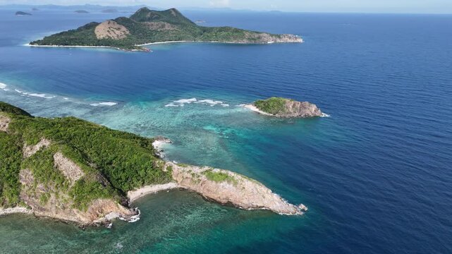 Pull-away drone shot of a rocky cape at Ile Island revealing nearby islands and turquoise waters washing over coastal reefs, Philippines