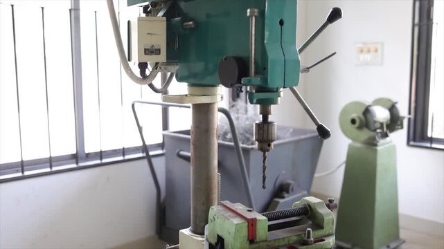 Vertical Drill Press Machine in Industrial Workshop with Metal Shavings and Bench Grinder Background
