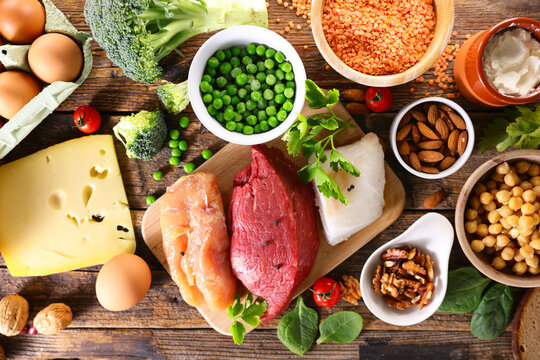 High protein food sources flat lay with raw meat, fish, eggs, legumes and nuts on wooden background