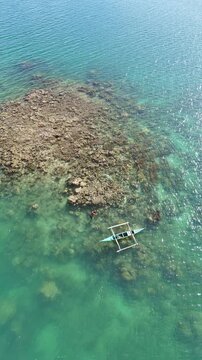 Portrait mode POI orbit drone shot of a fisherman swimming beside his small outrigger boat fishing in the reef at Linapacan, Palawan, Philippines