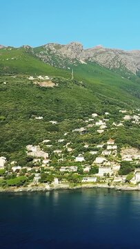 Scenic aerial shot of Erbalunga village nestled between lush green hills and the Mediterranean Sea on a clear day.