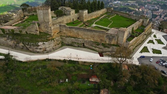 Aerial view of Lombard castle in Enna, showcasing ancient stone walls, lush greenery, and surrounding landscape with city structures in the background