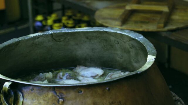 Chef lifts large pieces of meat with metal hook from boiling broth in ancient kazan for Uzbek plov