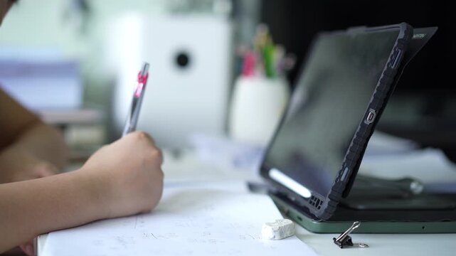 closeup computer tablet with hand child learn from home write on paper or young kid student doing homework to mathematics multiply calculate by study online class or people back to school learning