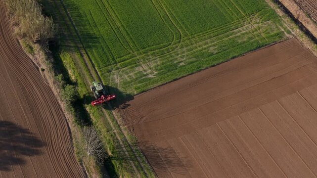 Aerial View of Cultivation: Witness a high-angle shot of a tractor at work in the field with parallel lines and different land shades, showcasing agricultural precision and dedication.