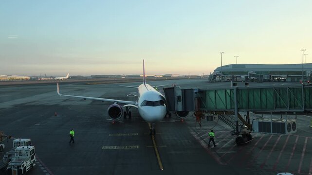 Passenger airplane parked at airport gate with jet bridge ground crew preparing aircraft for departure early morning light wide runway modern aviation travel scene