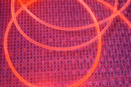 Lighting with interesting shapes, light guide, wire. Thick plastic flexible glowing wires with a soft red, cherry, pink glow are on a graphic pink plastic background with a silver reflection and small