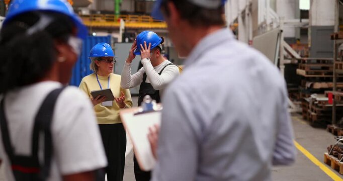 Diverse group of industrial workers and engineers having a briefing meeting in a factory. The female manager is holding a digital tablet while providing instructions to her professional team