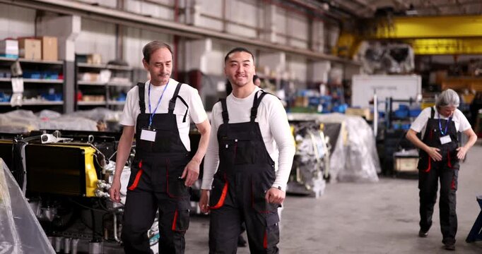 Multi ethnic group of happy mechanics and technicians dancing and celebrating while walking through a large industrial factory warehouse after a successful day of work and production
