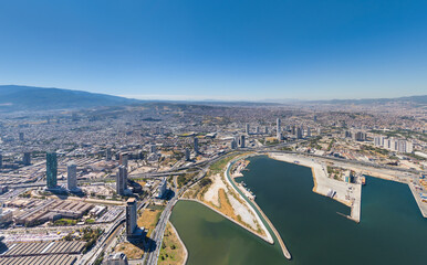 Obraz premium Izmir, Turkey. Panoramic view of Bayrakli district with modern skyscrapers, highway interchanges, and urban infrastructure. Partial view of coastline and green spaces. Summer daytime. Aerial view.