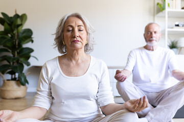 Fototapeta premium Senior couple practicing yoga and meditation at home for wellbeing