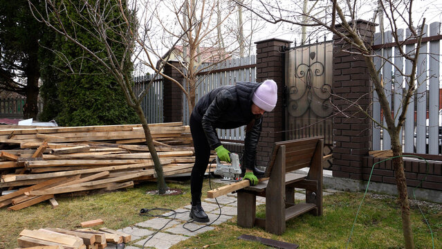 A woman works in the yard in the spring. A woman cuts and collects wood. A woman does spring yard chores.