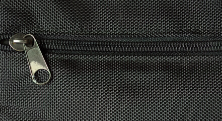 Macro close up of black zipper on textured fabric background with detailed metal slider and textile pattern. © Alexandr