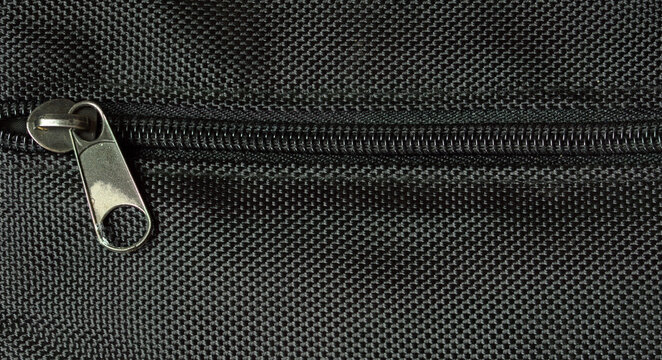 Macro close up of black zipper on textured fabric background with detailed metal slider and textile pattern.