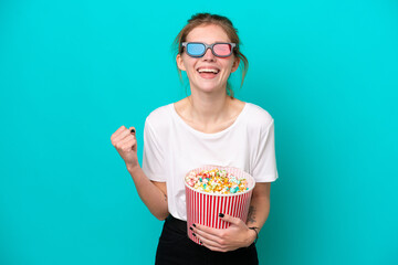 Young English woman isolated on blue background with 3d glasses and holding a big bucket of popcorns © luismolinero
