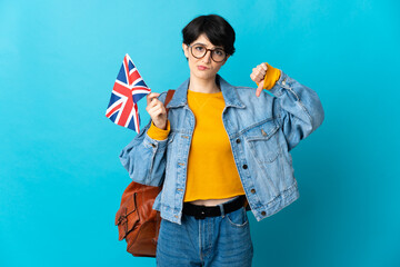 Woman holding an United Kingdom flag over isolated background showing thumb down with negative...