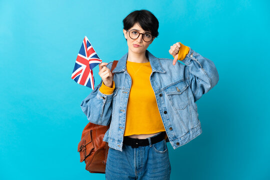 Woman holding an United Kingdom flag over isolated background showing thumb down with negative expression
