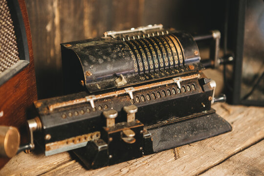 Vintage mechanical pinwheel calculator on a rustic wooden table. Distressed black metal arithmetic machine with brass details and number sliders, perfect for historical, office, or finance concepts.