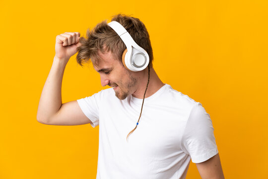 Young handsome blonde man isolated on yellow background listening music and dancing