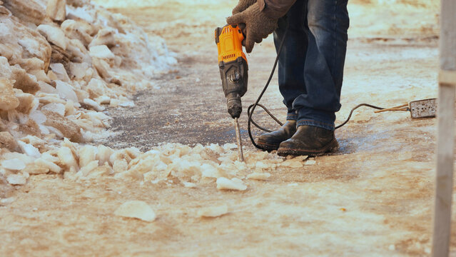 Worker using jackhammer to remove ice from a snow-covered sidewalk during winter