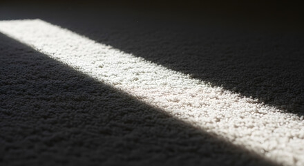 Fototapeta premium A beam of bright sunlight illuminates a textured dark carpet, creating a strong contrast between light and shadow.