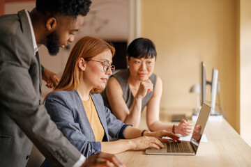 Diverse team of professionals analyzing financial report on laptop while collaborating in business...