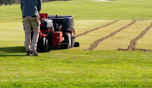 Groundskeeper aerating golf course green with professional turf maintenance machine on sunny day sports field care concept