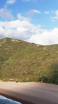 Scenic view of the Delta du Fango coastline in Corsica, featuring a pebbled beach, green hills, and a partly cloudy sky.