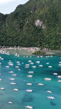 Aerial drone view of traditional banca boats anchored in the turquoise waters of Bacuit Bay near El Nido, Palawan, Philippines. Vertical