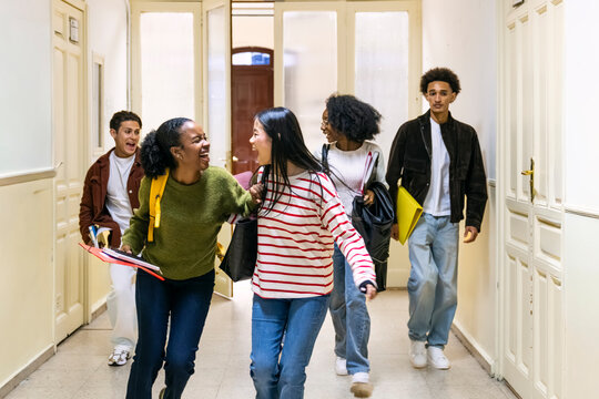 Diverse group of college students feeling happy walking and talking along university hallway, finishing class