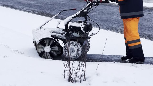 Worker clears snow with motorized snow blower. Yellow safety gear contrasts against white snow. Snow machine spins, pushing snow aside. Road remains clear after diligent effort