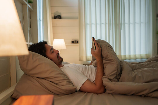 Japanese man lying in bed using smartphone with insomnia at night