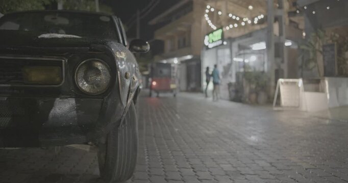 Close Up Headlight Of Old Retro Vintage Color Car Parked At Street Traffic on night street street near cafe bar in night time. Sri Lanka. Copy space blurred background