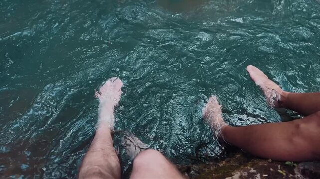 Couple relaxing with feet in river water in nature, Man and woman soaking legs in flowing stream enjoying refreshment, 4k slow motion