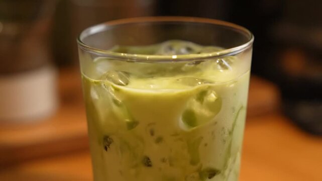 Pouring Iced Matcha Latte into a Glass with Ice Cubes, Refreshing Green Tea Beverage Preparation.