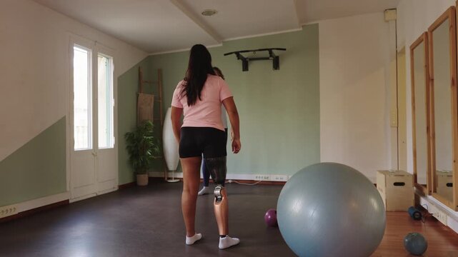 Amputee woman with prosthetic leg exercising in gym studio