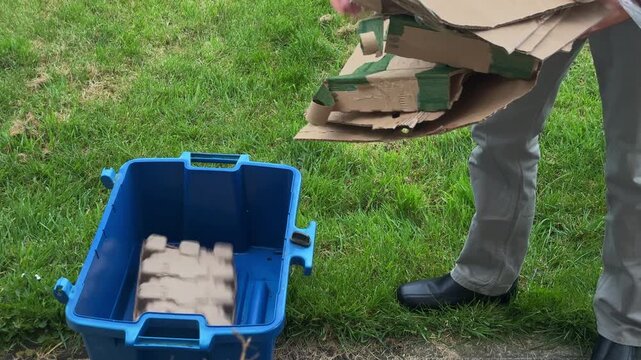 Person Placing Flattened Cardboard into Blue Plastic Recycling Box Outdoor, United Kingdom