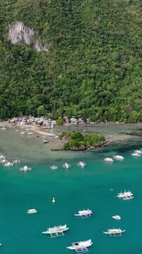 Aerial drone view of a small coastal village connected by a narrow sandbar and surrounded by shallow turquoise waters in El Nido, Palawan. Vertical