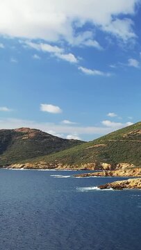 Scenic view of the rugged coastline and clear blue waters at Delta du Fango, with green hills and a partly cloudy sky. Ideal for nature, travel, and landscape concepts.
