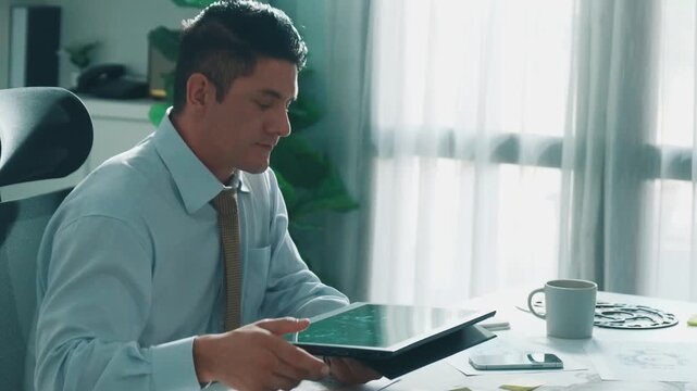 Professional engineer looking at phone while working on tablet with green screen at meeting table with turbine engine or jet engine sketch design and various metal gear scatter around. Alimentation.