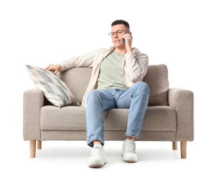 Young man talking by mobile phone on grey sofa against white background