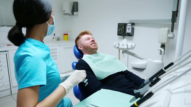 Young woman dentist examining a male patient's teeth with dental instruments in a modern clinic