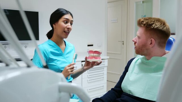 Dentist teaching a male patient correct tooth brushing on a jaw model in a dental clinic