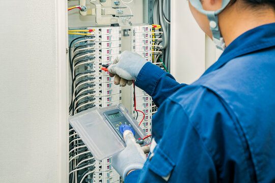分電盤の回路をデジタルテスターで点検する電気工事士の後ろ姿